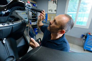 mechanic holding tablet while working on modern scooter © auremar
