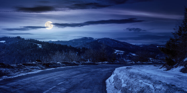 uzhanian pass in winter at night. old country road through mountains. beautiful countryside scenery with forested hills in full moon light