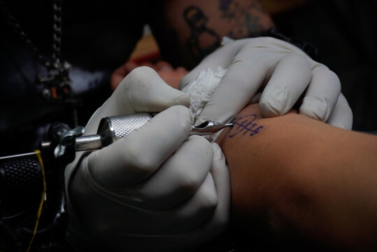 Tatuador realizando tatuaje en brazo en hombre joven