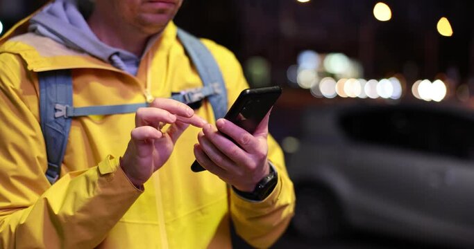 Male tourist traveler or orders taxi through taxi app on smartphone on city street