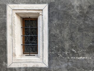 rectangular white window with bars on a gray stucco wall

