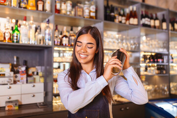 Young female worker at bartender desk in restaurant bar preparing coctail with shaker. beautiful young woman behind bar making coctail