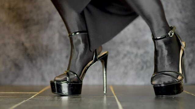 a young woman with sporty sexy legs wears shiny black stockings and high-heeled black stilettos and does a fashion show with the shoes after that she walks out of the frame, dolly slide