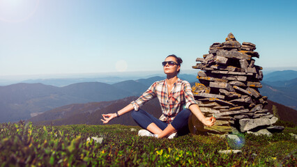 Young woman exercises yoga in the mountains. Travel relax exercises yoga on mountain peak.