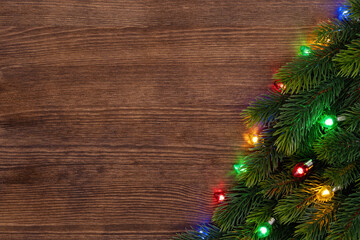 Christmas theme. Christmas tree with glowing retro garland. Nostalgic multicolor illuminated garland on a brown wooden background with copy space.