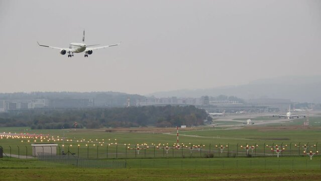 A passenger airplane is landing on a runway illuminated by lights, A380-800 is taxiing in the background