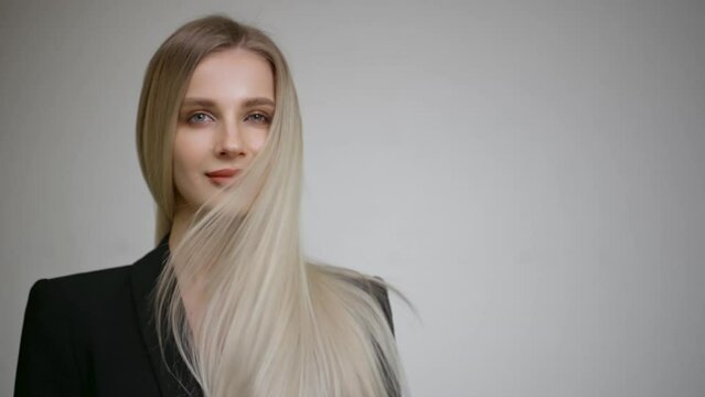 Slow motion of the flying hair of a charming blonde. Grey background.