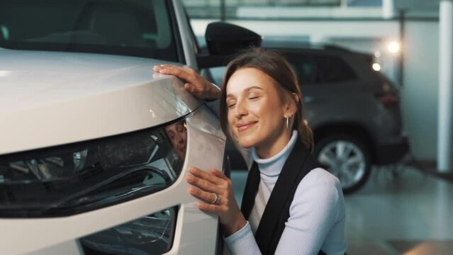 a happy woman inspects the paintwork of her car in a car dealership