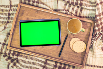 Digital tablet with green screen and stylus pencil, a cup of coffee. Work at home concept. Wooden...