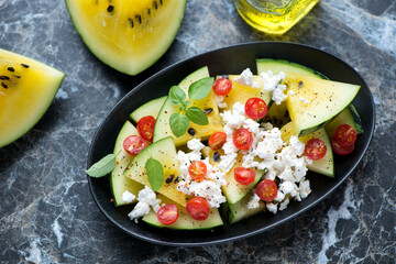 Salad with yellow watermelon, goat cheese and red cherry tomatoes on a black marble background, elevated view, horizontal shot