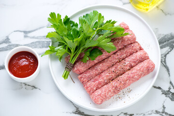 Raw serbian cevapi or cevapcici sausages with fresh parsley on a white marble background,...