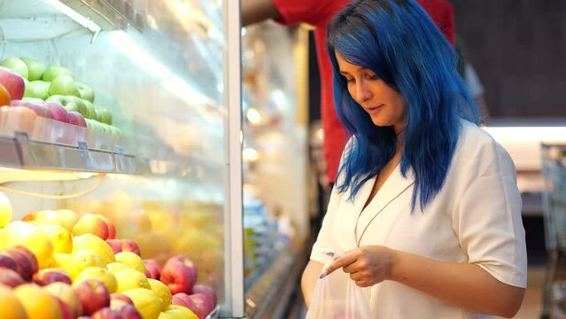 Customer woman choosing apples in budget supermarket, take one from heap and put good in plastic bag. The picky lady puts back the fruit she doesn't like. Selective focus shot