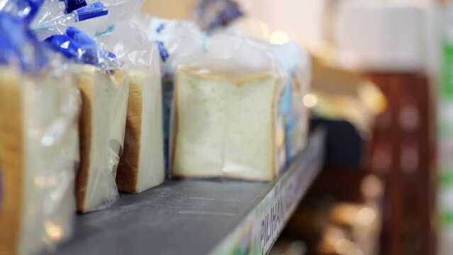 Sliced wheat bread for toasts packed in individual plastic bags, customer woman pick one from shelf, close up shot with selective focus. Daily shopping at budget supermarket