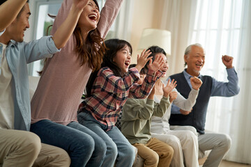 three generation asian family watching soccer game telecast on tv together at home