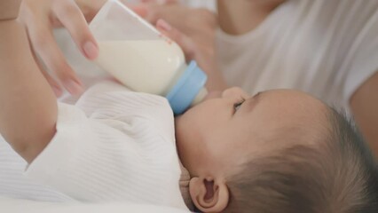 Closeup view of Young asian mother feeding her little cute baby daughter with bottle on bed.Asian young mother See also baby and asian newborn baby suck milk from bottle and sleep on white bed
