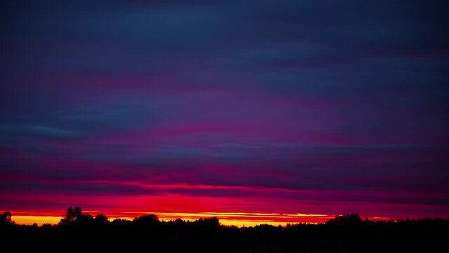 Amazing colorful sunset above the forest trees with purple and red clouds flowing - time lapse