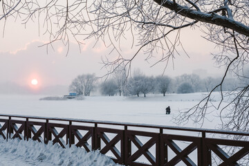Beautiful winter landscape. A fisherman in the snow. Sunset on the river