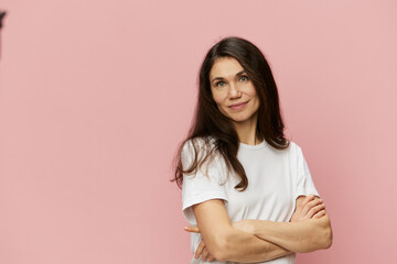 horizontal portrait of a cute, attractive woman on a pink background in a clean white t-shirt smiling pleasantly at the camera and folding her arms on her chest