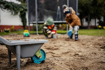 Selective focus on wheelbarrow toy full of sand with boys playing in sand in a background.