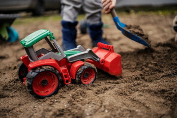 An excavator toy with a boy in background digging a sand.