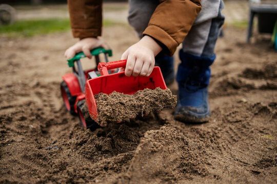 Close up of a boy digging sand with excavator toy.