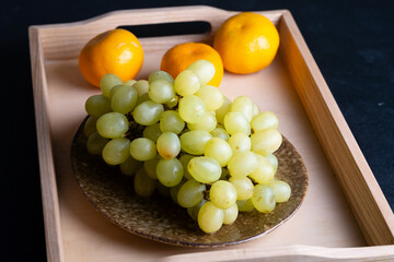 Wooden tray with grape on plate, tangerines.