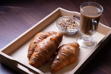 Wooden tray with a cup of  coffee, muesli and with a fresh croissants on a brown table