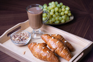 Wooden tray with a cup of  coffee, muesli and with a fresh croissants on a brown table