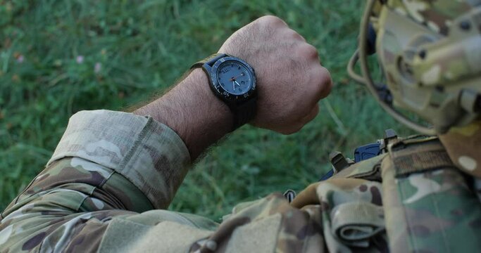 Close-up unrecognizable male soldier in camouflage uniforms getting ready for military exercises or battle. Detailed shot of military man checking time, looking at watch. Ukrainian russian war