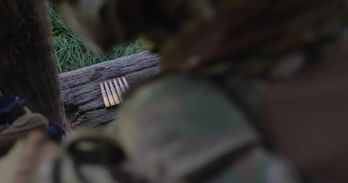 Cartridges for a machine gun lie in a row on a wooden surface. A human hand in a tactical glove takes them and charges them. Ukrainian army, war