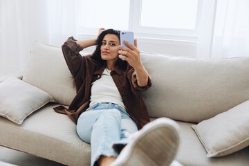 Woman blogger with phone lies at home on the couch and works freelancer online, selfie