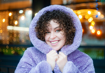 Smiling curly haired woman in trendy violet posing on festive christmas background