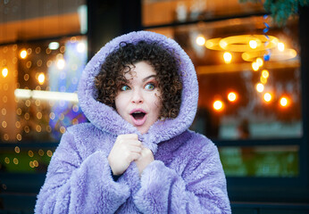 Smiling curly haired woman in trendy violet posing on festive christmas background