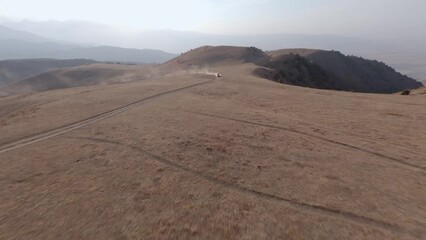 SUV car speed race riding towards on dirt road at desert sand mountain with blue sky aerial view. FPV sports drone shot extreme dust automobile drive journey transportation offroad rally tourism 4k