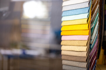 Fabric swatches in different colors are stacked for selection. A variety of shades of upholstery material for furniture and interior. Fabric texture close up. A set of multi-colored rolls of material.