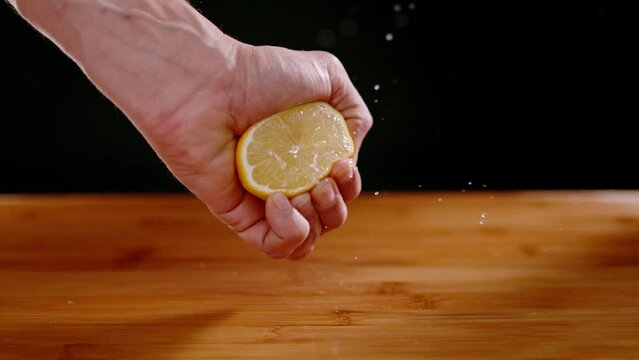 Person hand squeezing fresh lemon with squirting juices, super slow motion