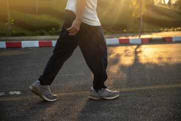 man walking on road with sun light flare ,close up on shoe jogging workout wellness after work