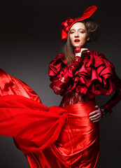 Young beautiful woman in a red lace suit and hat. Stylish blonde in a flowing skirt, a symbol of passion and energy.