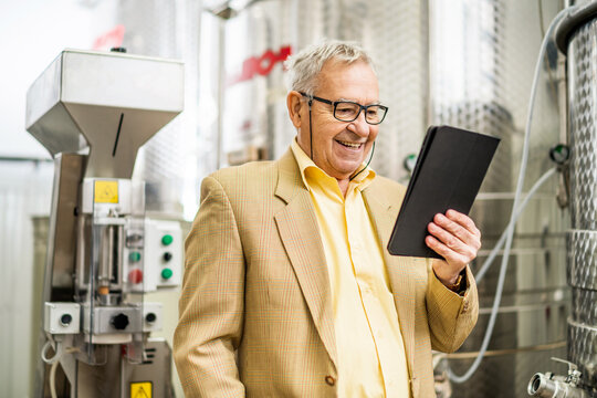 Portrait of happy senior man who owns winery. He is standing beside wine storage tanks and examining cooling process. - Powered by Adobe