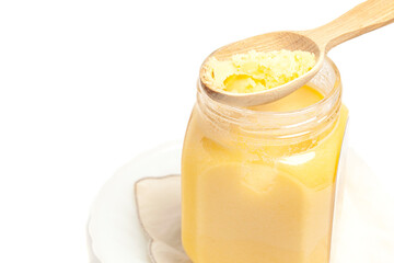 Ghee in jar and wooden spoon isolated on white background