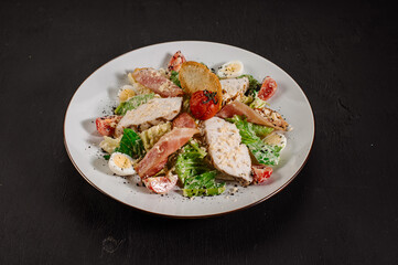 Tasty fresh salad ceasar with ham and vegetables on black background