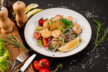Tasty salad with shrimps, herbs and vegetables on black background