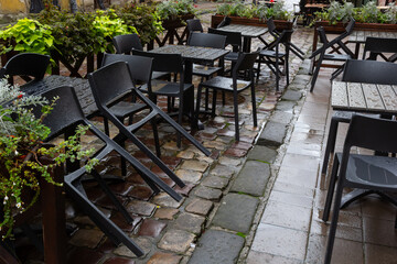Empty wet wooden table and chairs on terrace of outdoor cafeteria during rain. Street city life in rain