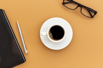 Office table with cup of hot black coffee and notebook