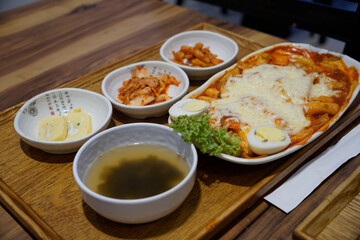 Cheesy tteokbokki served with kimchi and side dishes 
