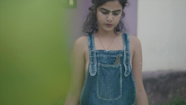 Camera revealing woman artist looking down with bohemian look and make-up wearing denim dungarees and revealing body, Slow motion