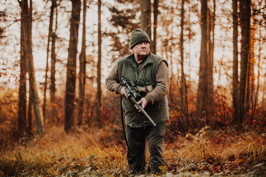 Autumn hunting season, hunter with rifle looking out for some wild animal in the wood or forest, outdoor sports concept