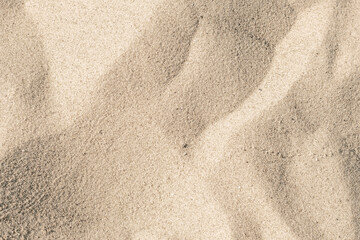 Close-up of a sandy beach. Background with sand unevenly swept away by wind and waves into small dunes. Background for a cover or design on the theme of travel.