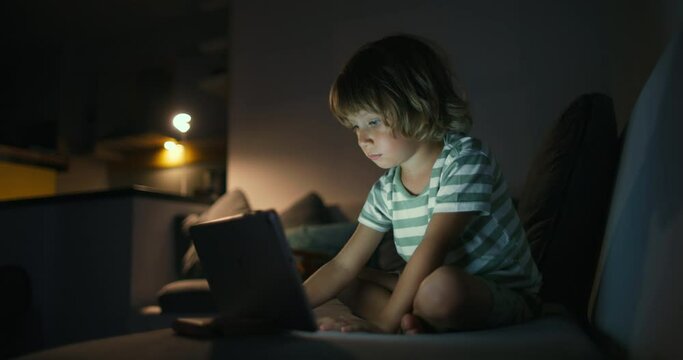 Cute small kid boy in living room using funny editing application on digital computer tablet, enjoying cool video or photo content in social network, playing online games, communicating distantly.