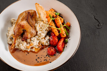 Dish of oatmeal with baked quail and vegetables on wooden background